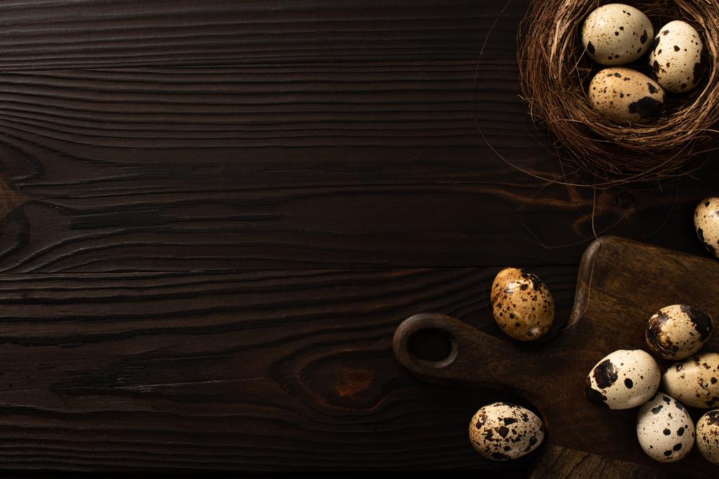 top view of quail eggs in brown nest and on chopping board on dark wooden background - Photo, Image