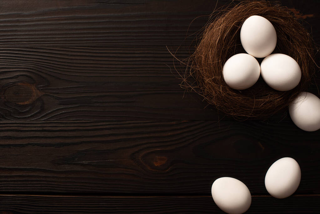 верхний вид белых куриных яиц в гнезде и на коричневом деревянном фоне
 - Фото, изображение
