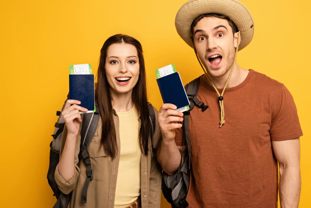 ζευγάρι ενθουσιασμένοι ταξιδιώτες με σακίδια που κατέχουν διαβατήρια και εισιτήρια σε κίτρινο - Φωτογραφία, εικόνα