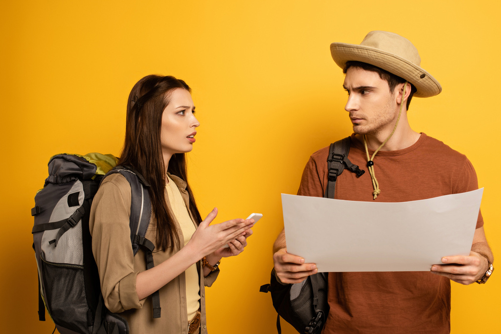 casal de turistas confusos com mochilas e smartphones olhando para o mapa no amarelo
 - Foto, Imagem