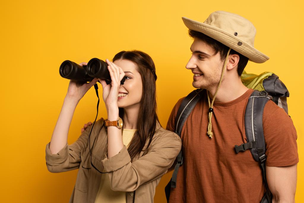 couple of smiling travelers with backpack and binoculars on yellow - Photo, Image