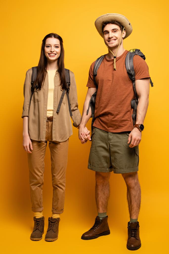coppia di turisti felici con zaini che si tengono per mano sul giallo
 - Foto, immagini