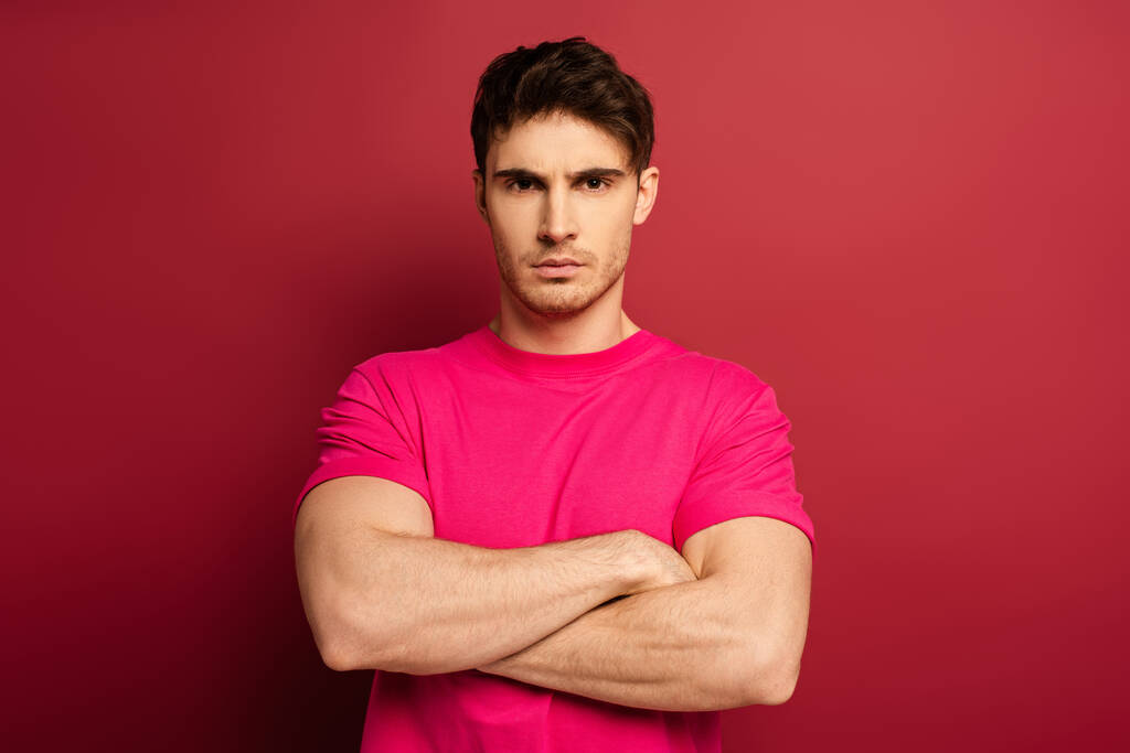 retrato de hombre serio con brazos cruzados en camiseta rosa sobre rojo
 - Foto, Imagen