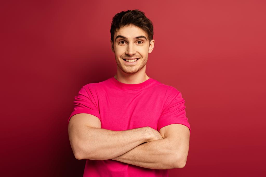 portret van lachende man in roze t-shirt met gekruiste armen op rood - Foto, afbeelding