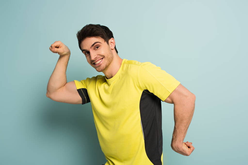 Lihaksikas hymyilevä urheilija elehtii keltaisessa t-paidassa sinisellä
 - Valokuva, kuva