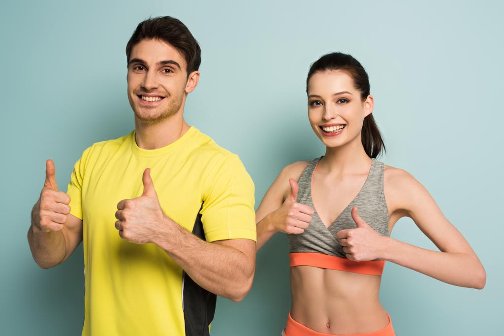 χαρούμενο αθλητικό ζευγάρι στέκεται σε αθλητικά ρούχα δείχνει τους αντίχειρες επάνω στο μπλε - Φωτογραφία, εικόνα