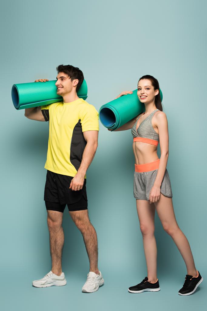 mosolygó sportos pár kezében fitness szőnyeg kék - Fotó, kép