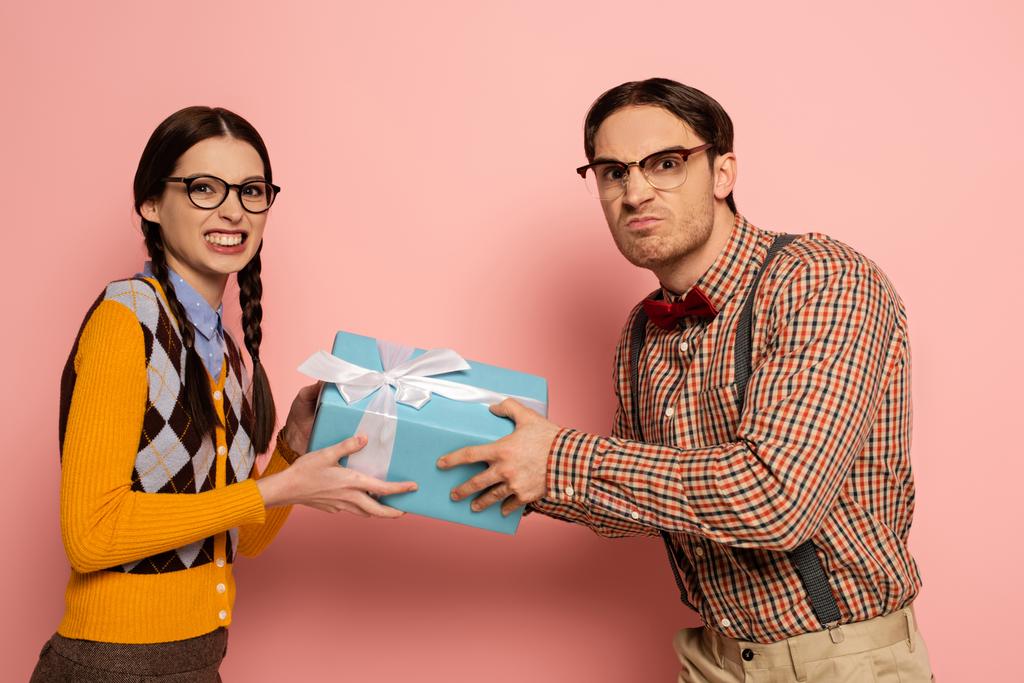 δύο θυμωμένοι σπασίκλες με γυαλιά που κρατούν ένα δώρο στο ροζ - Φωτογραφία, εικόνα