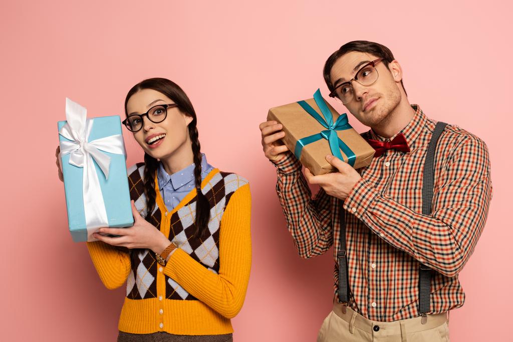 couple of emotional nerds in eyeglasses holding gifts on pink - Photo, Image