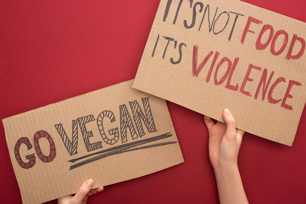 μερική άποψη της γυναίκας κρατώντας χαρτονένια σημάδια με πάει vegan και δεν του τροφίμων της βίας επιγραφές στο κόκκινο φόντο - Φωτογραφία, εικόνα