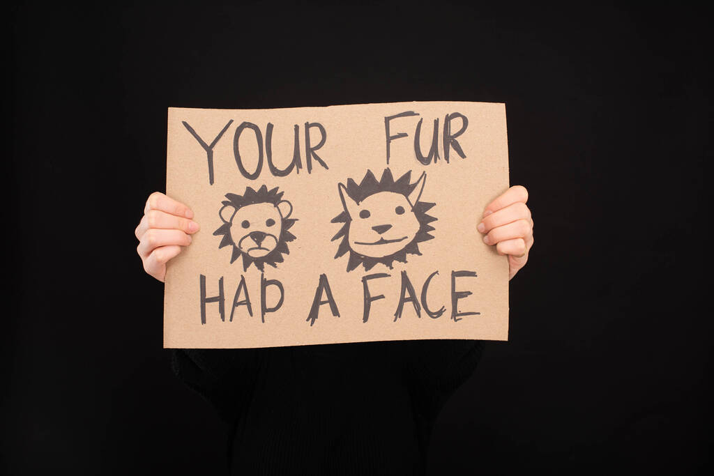 vue partielle de la femme tenant une pancarte en carton avec votre fourrure avait une inscription sur le visage isolé sur noir
 - Photo, image