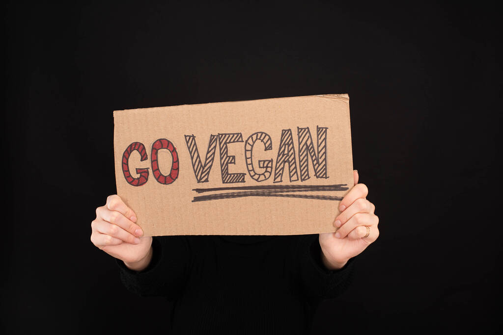 partial view of woman holding sign with go vegan inscription isolated on black - Photo, Image