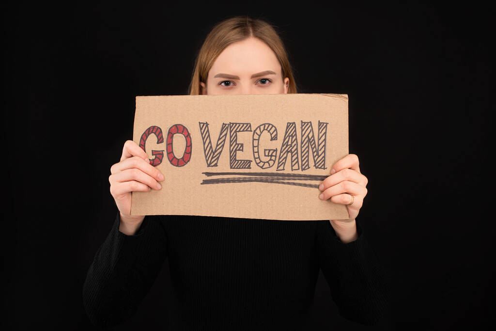 mulher com rosto obscuro segurando papelão com go inscrição vegan isolado em preto
 - Foto, Imagem