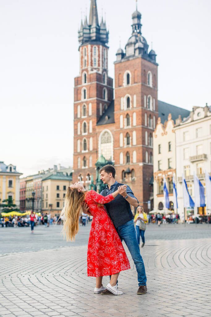 una joven pareja está elegantemente vestida, una chica con un vestido rojo, un hombre con una camisa azul y pantalones azules, caminar por las calles en Cracovia Polonia
 - Foto, imagen