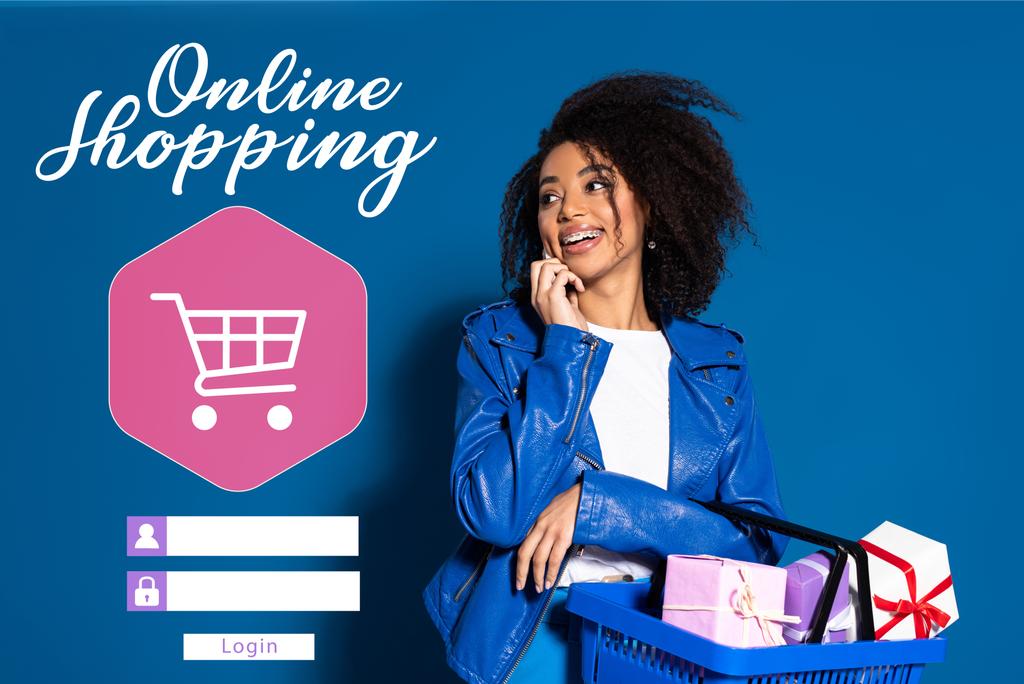 sonriente mujer afroamericana sosteniendo cesta de la compra con regalos y hablando en el teléfono inteligente sobre fondo azul, ilustración de compras en línea
  - Foto, imagen