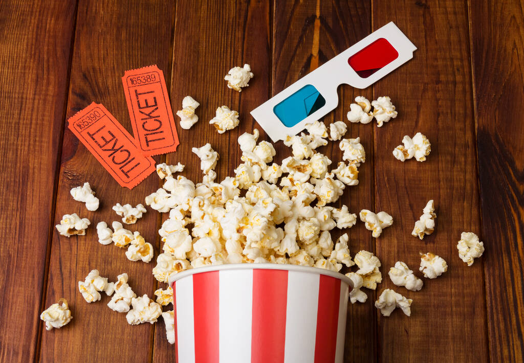 Volný popcorn v pruhované krabici, dva lístky do kina a 3D brýle na dřevěném pozadí - Fotografie, Obrázek