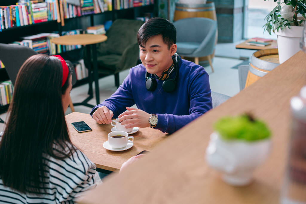 Jovem alegre sentado com uma xícara de café e olhando para a jovem na frente dele
 - Foto, Imagem
