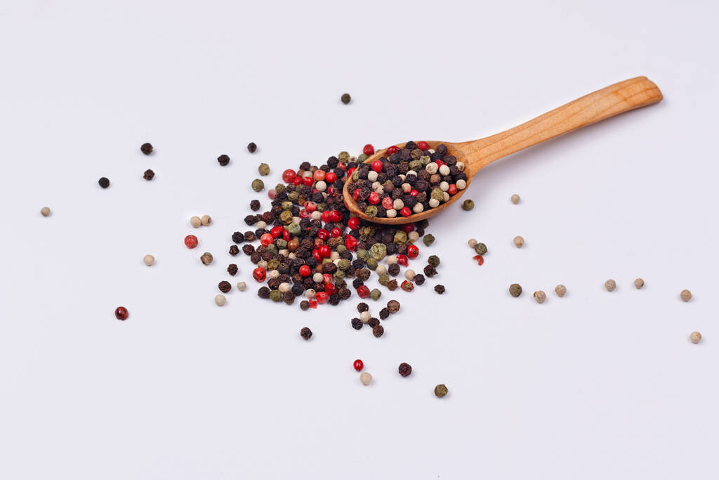 A mixture of multi-colored pepper in a wooden spoon on a white background. Isolate - Photo, Image