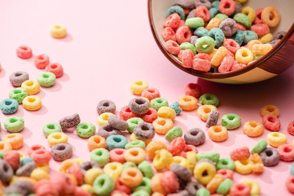 enfoque selectivo de cereales de desayuno de colores brillantes dispersos desde el tazón sobre fondo rosa
 - Foto, Imagen