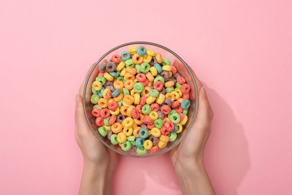 vista recortada de la mujer sosteniendo cereales de desayuno de colores brillantes en un tazón sobre fondo rosa
 - Foto, Imagen