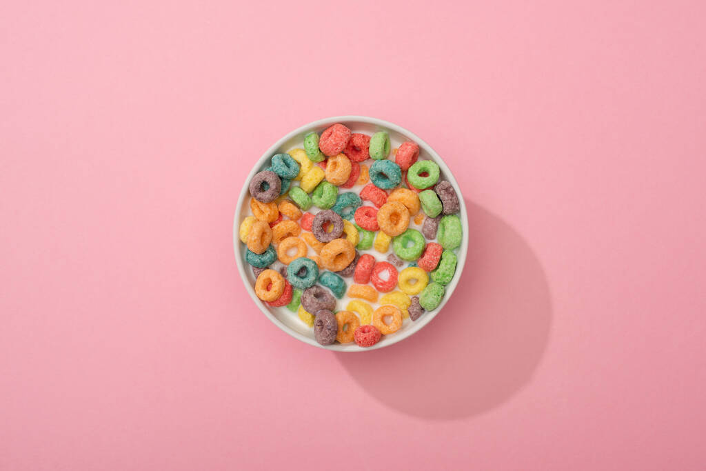 Draufsicht auf helle bunte Frühstückszerealien in Schüssel auf rosa Hintergrund - Foto, Bild
