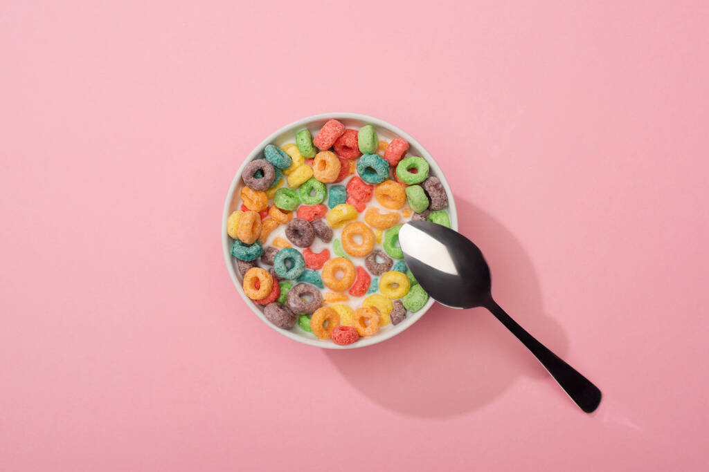 ピンクの背景にスプーンでボウルに鮮やかなカラフルな朝食シリアルのトップビュー - 写真・画像