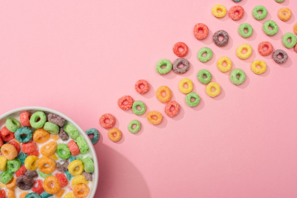 top view of bright colorful breakfast cereal with milk in bowl and around on pink background - Photo, Image
