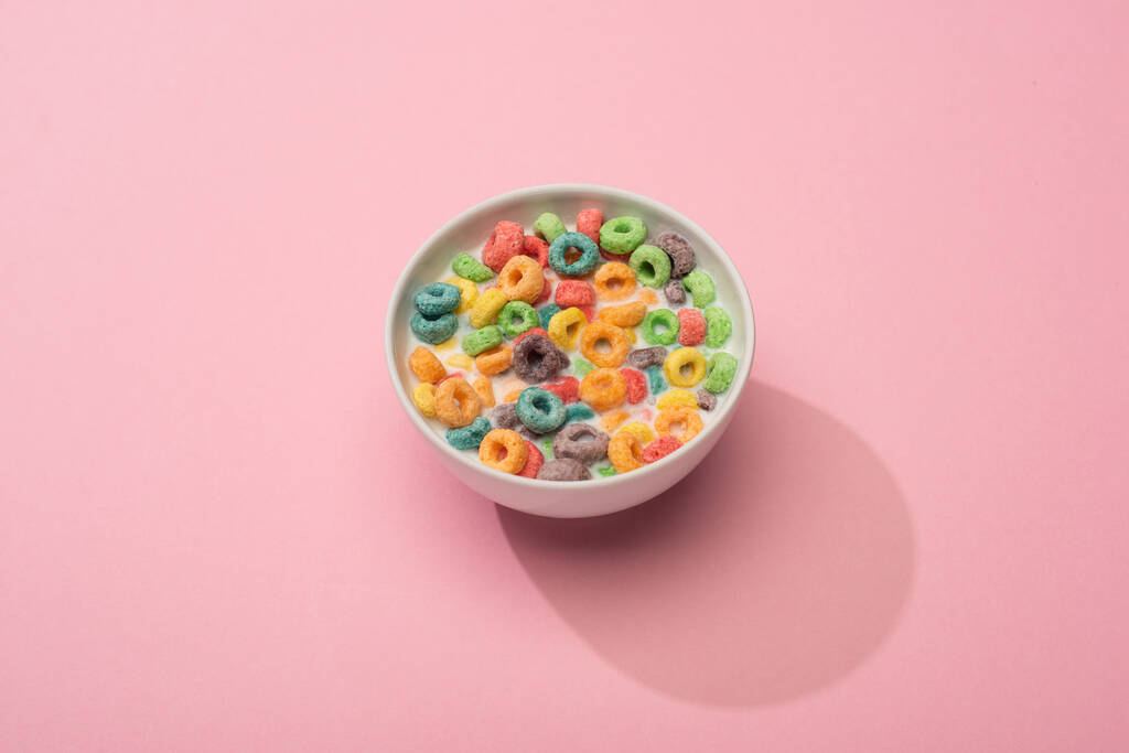 φωτεινό πολύχρωμο πρωινό δημητριακά με γάλα σε μπολ σε ροζ φόντο - Φωτογραφία, εικόνα