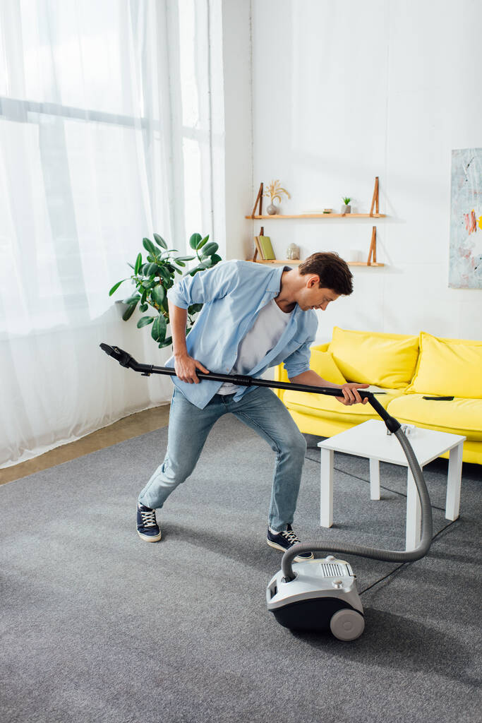 Hombre sosteniendo cepillo de aspiradora mientras limpia en la sala de estar
 - Foto, imagen