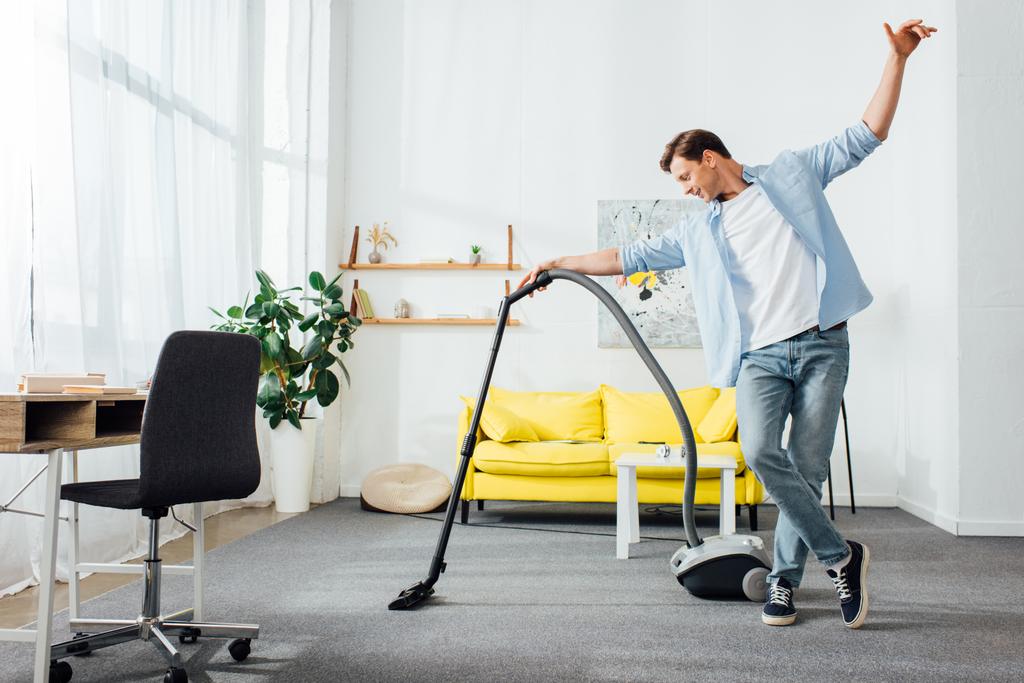 Handsome man cleaning carpet with vacuum cleaner in living room - Photo, Image