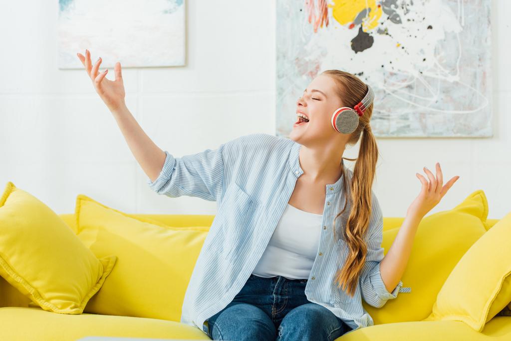 Belle femme chantant en écoutant de la musique dans les écouteurs sur le canapé à la maison
  - Photo, image