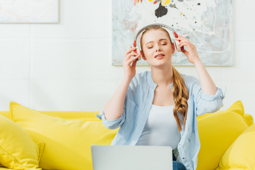 Piękna kobieta słuchająca muzyki w słuchawkach w pobliżu laptopa w domu - Zdjęcie, obraz