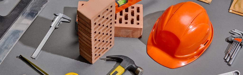 plano panorámico de ladrillos, martillo, llaves angulares, casco naranja, pinzas y cuchillo de masilla sobre fondo gris
 - Foto, imagen