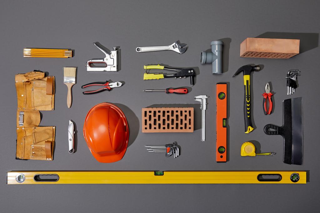 tendido plano con ladrillos, casco naranja, cinturón de herramientas y herramientas industriales sobre fondo gris
 - Foto, Imagen