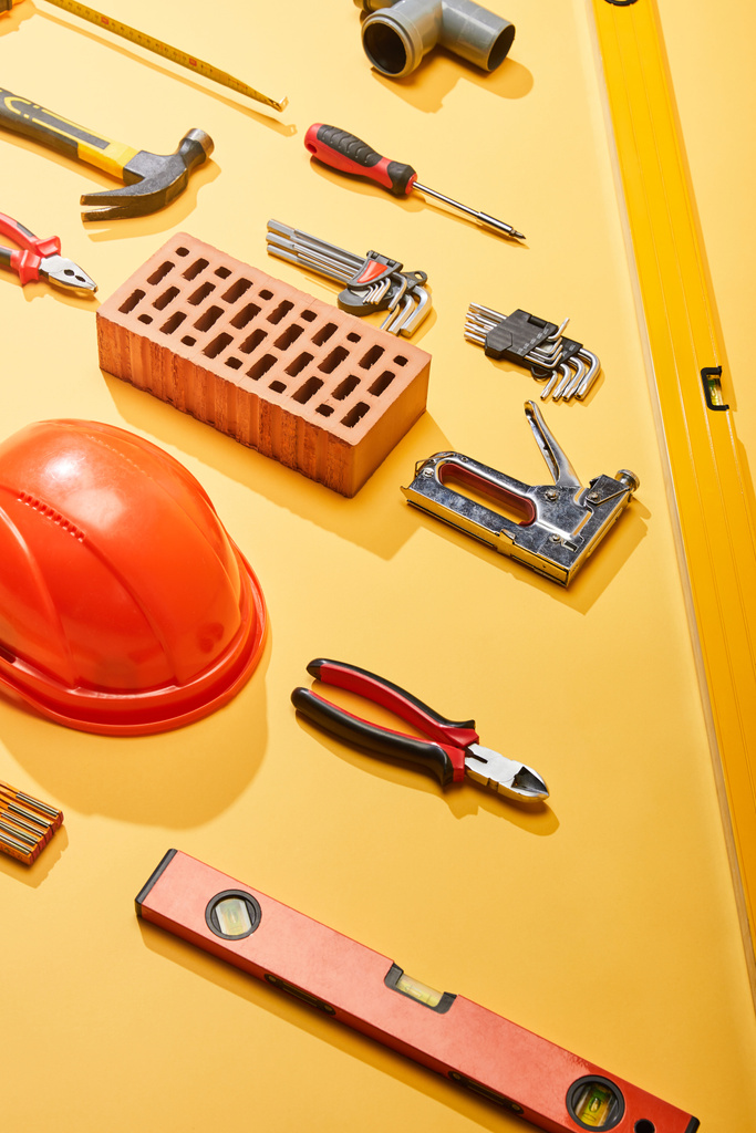 tendido plano con herramientas industriales, ladrillo y casco sobre fondo amarillo
 - Foto, imagen