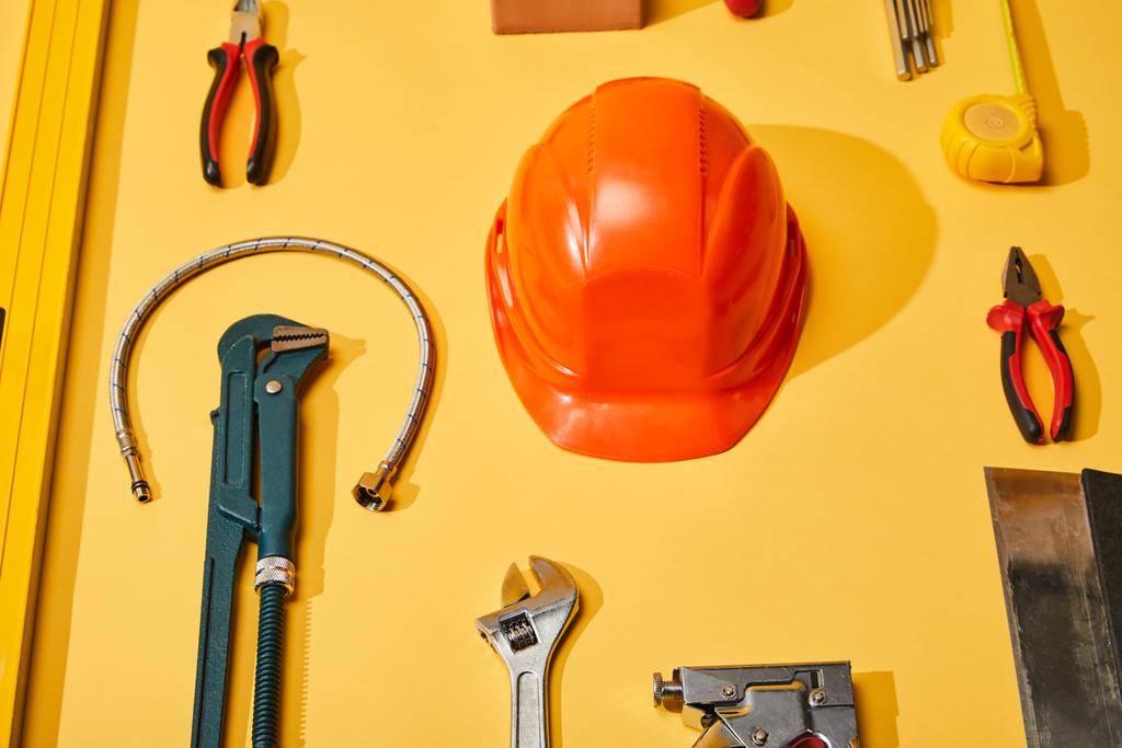 flat lay with helmet, calipers, monkey wrench, putty knife, plumbing hose, spirit level, measuring tape and angle keys on yellow background - Photo, Image