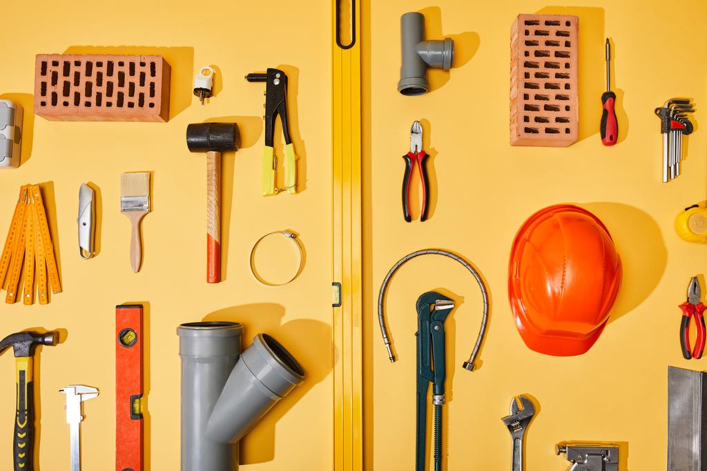 flat lay com ferramentas industriais, tijolos e capacete no fundo amarelo
 - Foto, Imagem