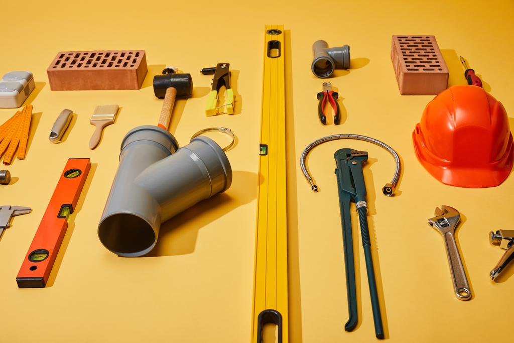 visão de alto ângulo de ferramentas industriais, tijolos e capacete no fundo amarelo
 - Foto, Imagem