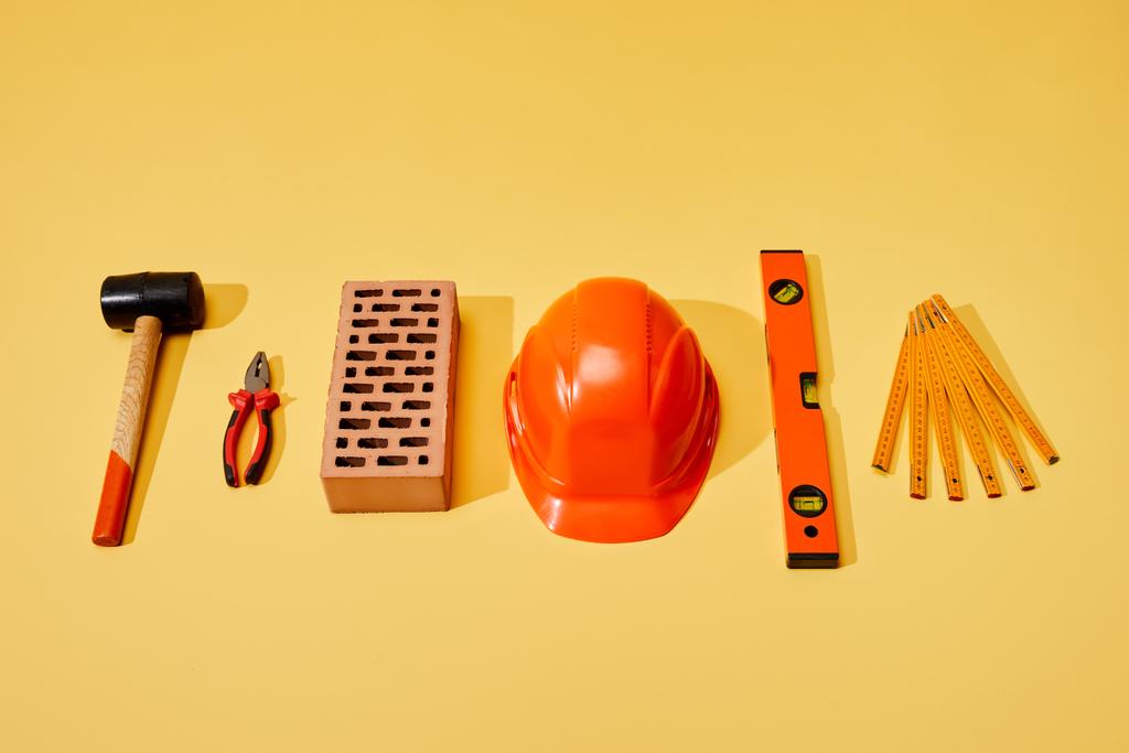 flat lay with hammer, pliers, brick, helmet, spirit level and folding ruler on yellow background - Photo, Image