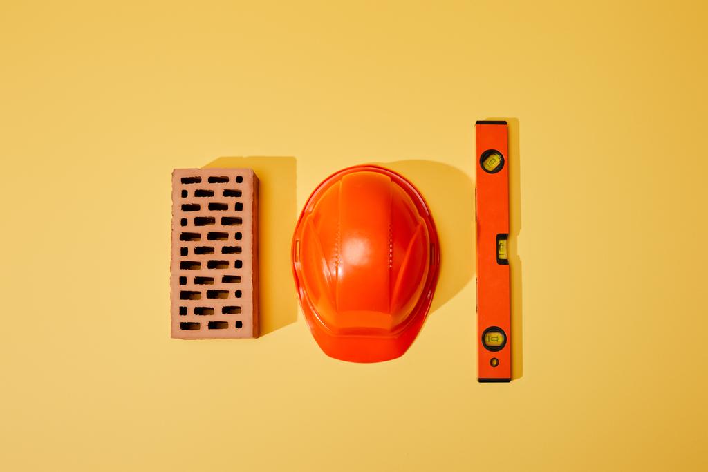 вид сверху на кирпич, оранжевый шлем и уровень духа на желтом фоне
 - Фото, изображение