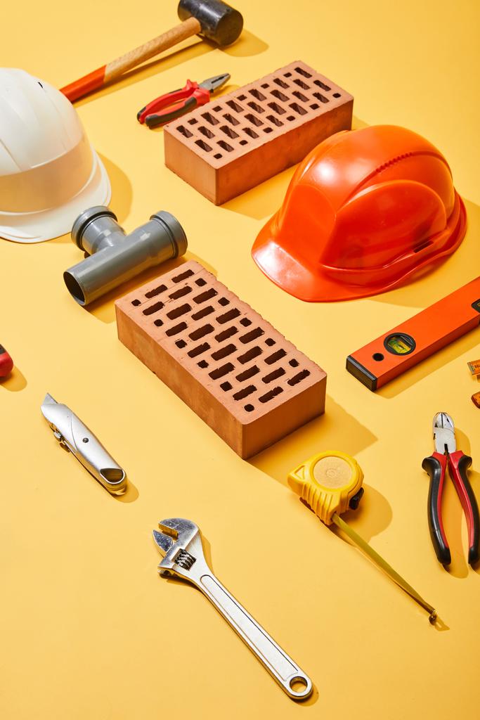 visão de alto ângulo de tijolos, capacetes e ferramentas industriais no fundo amarelo
 - Foto, Imagem