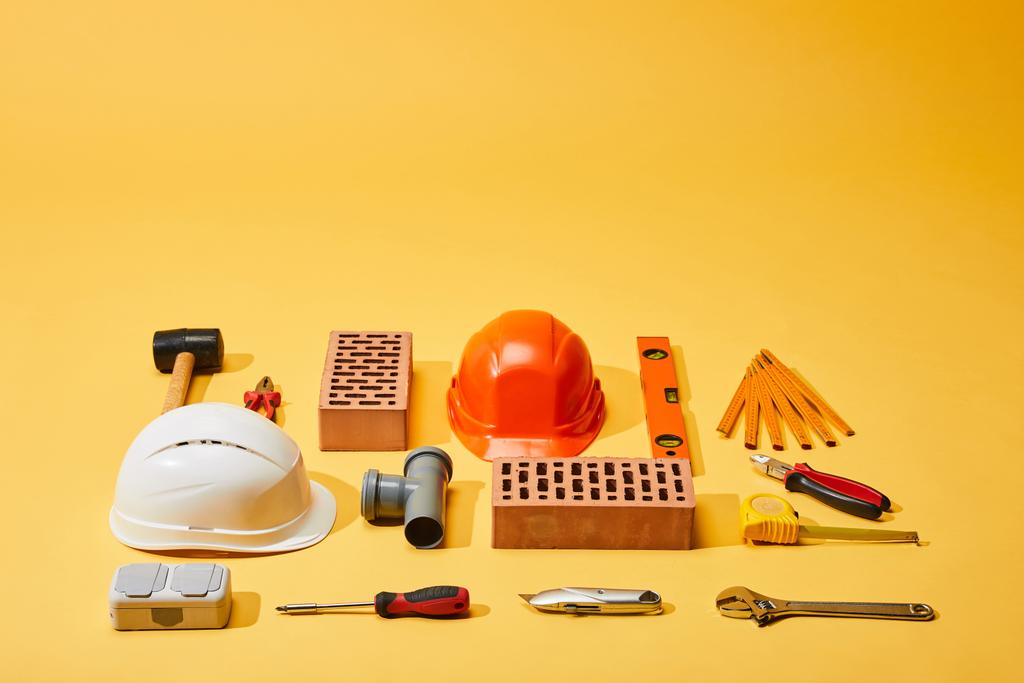 vista de alto ángulo de ladrillos, cascos y herramientas industriales sobre fondo amarillo
 - Foto, Imagen