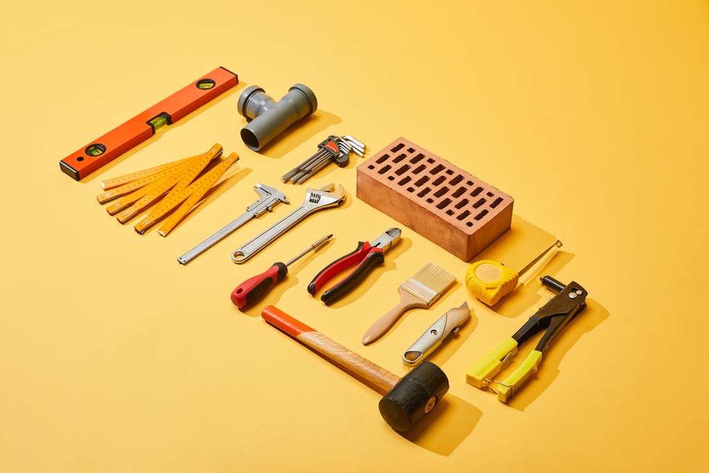 visão de alto ângulo de ferramentas industriais e tijolo no fundo amarelo
 - Foto, Imagem