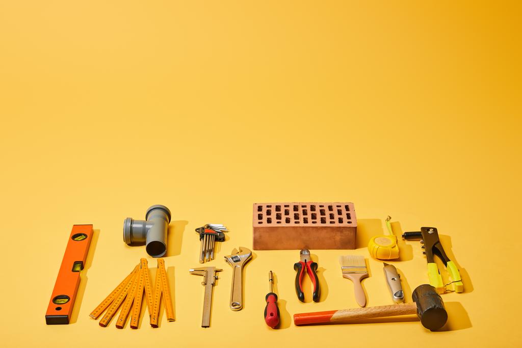 επίπεδο lay με βιομηχανικά εργαλεία και τούβλο σε κίτρινο φόντο - Φωτογραφία, εικόνα