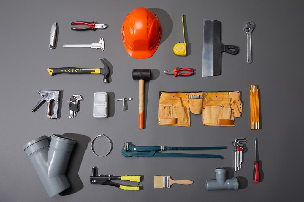 flat lay of industrial tools, helmet, measuring tape, tool belt and brush on grey background - Photo, Image