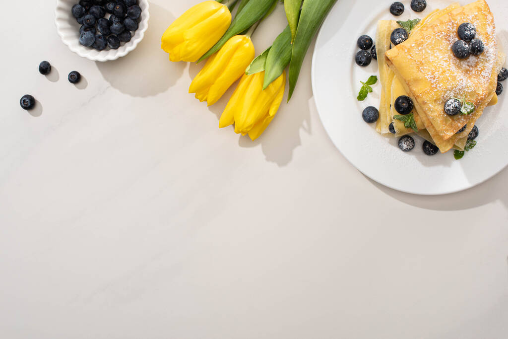 вид зверху смачних креветок біля миски з чорниці та жовтих тюльпанів на сірому фоні
 - Фото, зображення