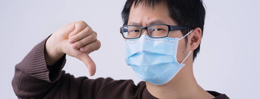 Porträt eines jungen asiatischen Mannes, der Nein zur Coronavirus-Infektion sagt, mit medizinischer blauer Gesichtsmaske auf weißem Hintergrund, Nahaufnahme, Nahaufnahme. - Foto, Bild