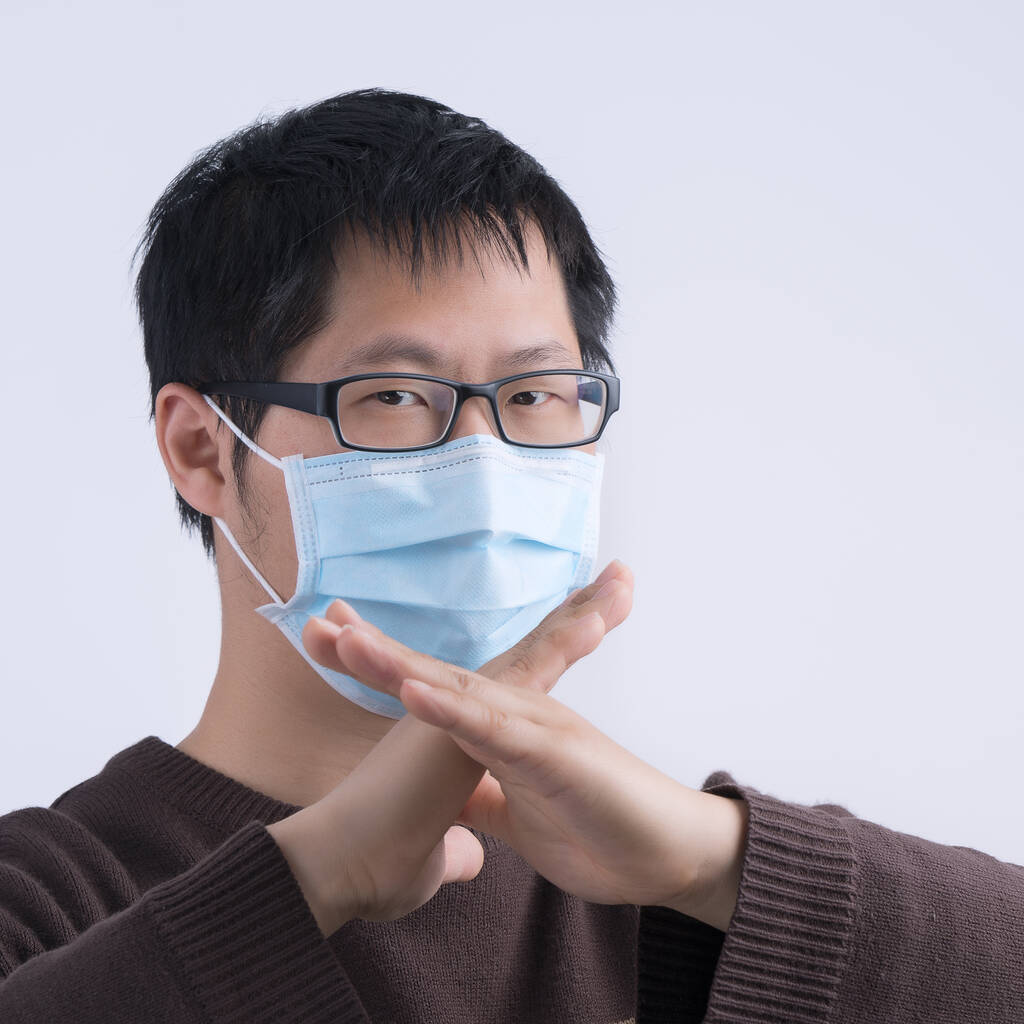 Retrato de un joven asiático, diciendo no a la infección por coronavirus con el uso de la máscara médica quirúrgica azul de la cara aislada en el fondo blanco, de cerca, de cerca
. - Foto, Imagen