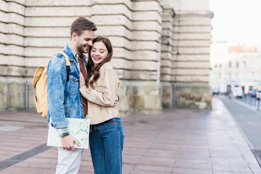 Focus selettivo della coppia felice che abbraccia e sorride con la mappa in città
 - Foto, immagini