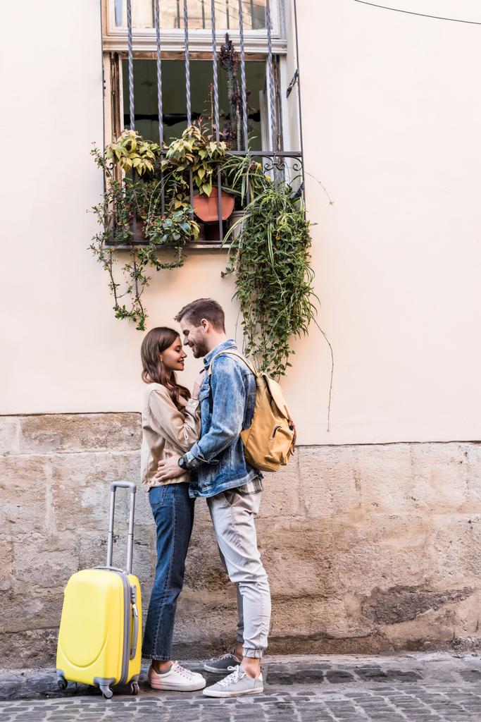 Пара з рюкзаком і валіза обіймається біля стіни в місті
 - Фото, зображення